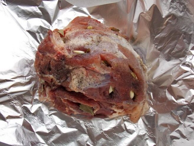 Wrapping the Pork Tightly in Foil to Keep it Juicy A piece of seasoned pork being wrapped tightly in aluminum foil on a wooden board.