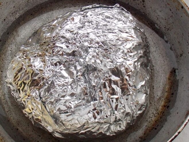 Placing the Foil-Wrapped Pork in a Cast-Iron Skillet for Roasting Foil-wrapped pork placed in a black cast-iron skillet with a little water at the bottom.