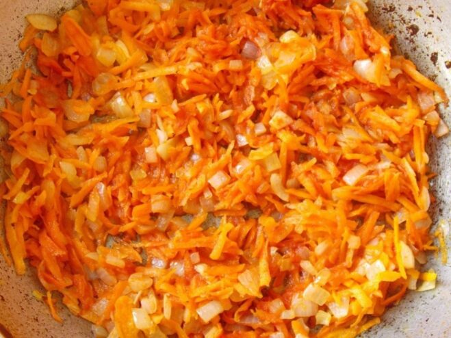 Sautéing Onions and Carrots for the Sauce Base Finely chopped onions and grated carrots being sautéed in a pan to create a flavorful base.