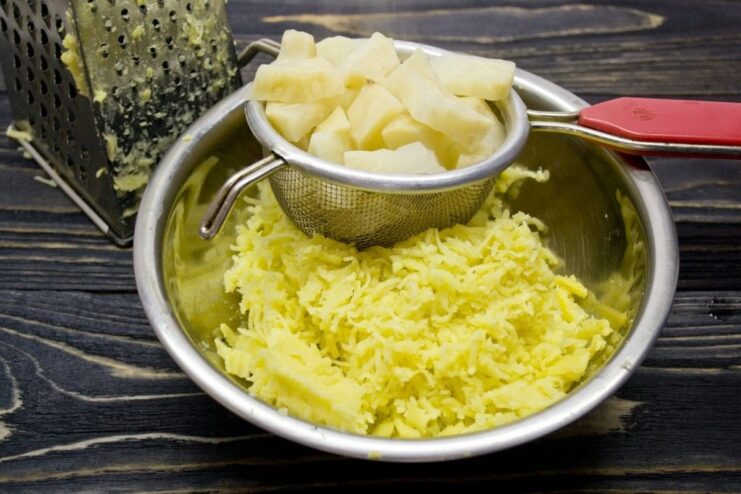 Using a Potato Ricer for a Smooth Gnocchi Dough Base Cooked potatoes and celeriac being pushed through a potato ricer into a bowl.