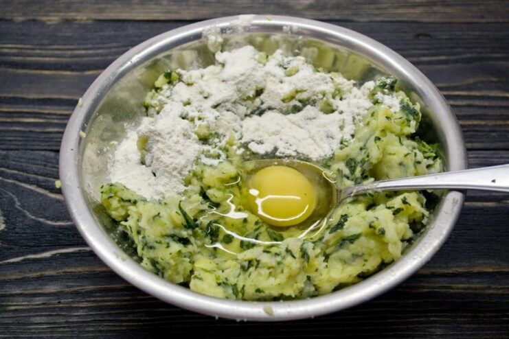 Combining All Ingredients to Form the Gnocchi Dough Egg, flour, and spices being added to the vegetable mixture in a bowl to make gnocchi dough.