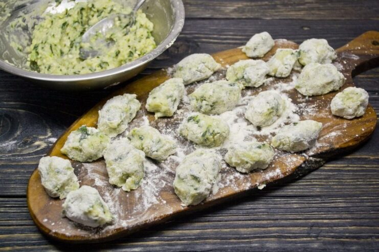 How to Shape Gnocchi: Rolling and Cutting the Dough A long rope of gnocchi dough on a floured surface being cut into small, pillow-like pieces.