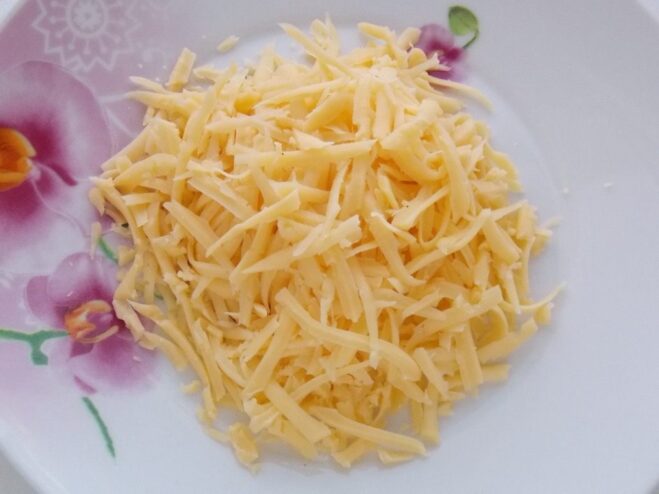 Grating a block of semi-hard cheese for the filling Close-up of hands grating a block of yellow cheese on a box grater.
