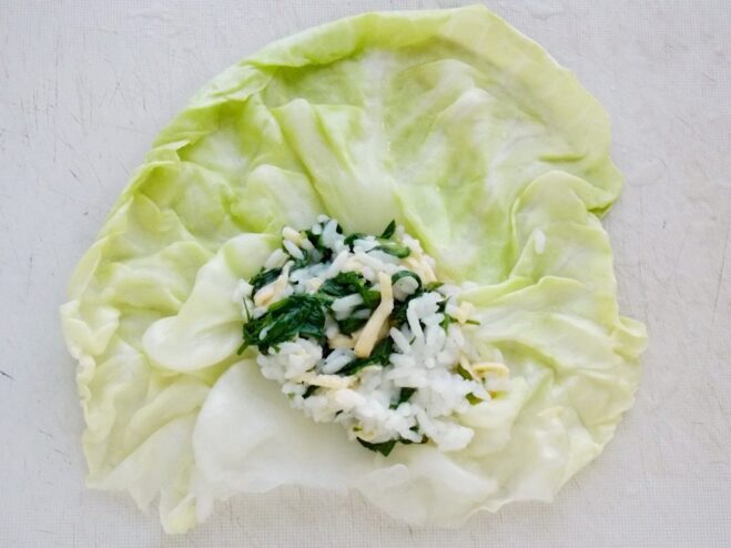 Step-by-step: How to fill cabbage rolls A softened cabbage leaf laid flat with a spoonful of spinach and rice filling on top.