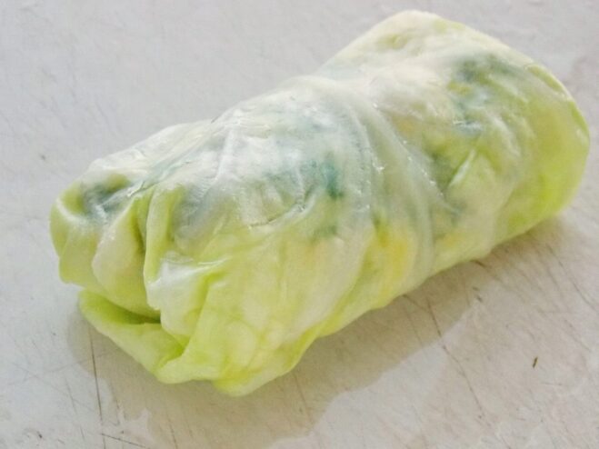 The technique for rolling perfect golubtsy Hands folding a cabbage leaf over the filling to create a neat cabbage roll.