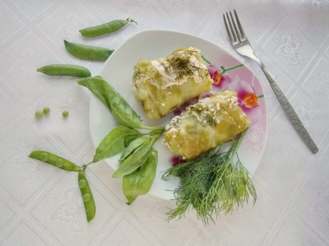 A plate of cooked golubtsy with spinach, served with a dollop of sour cream and fresh herbs.