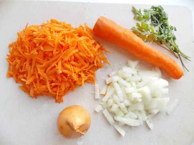 Preparing the vegetable base for the zucchini stuffing Chopped onions and grated carrots on a cutting board, ready for sautéing.