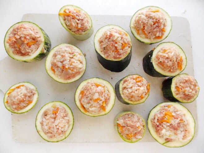 Filling the prepared zucchini cups with the savory stuffing Hollowed-out zucchini rounds being filled with the meat and rice mixture.