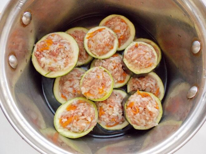 Arranging the stuffed zucchini in a pot for cooking Stuffed zucchini rounds arranged snugly in a large cooking pot, ready to be stewed.