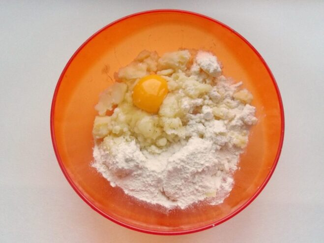 Preparing the Potato Dough for Zrazy A bowl of mashed potatoes with an egg, flour, salt, and pepper ready to be mixed.