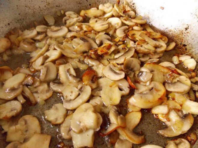 Sautéing Mushrooms and Onions for the Filling Sliced mushrooms and chopped onions being sautéed in a frying pan until golden.