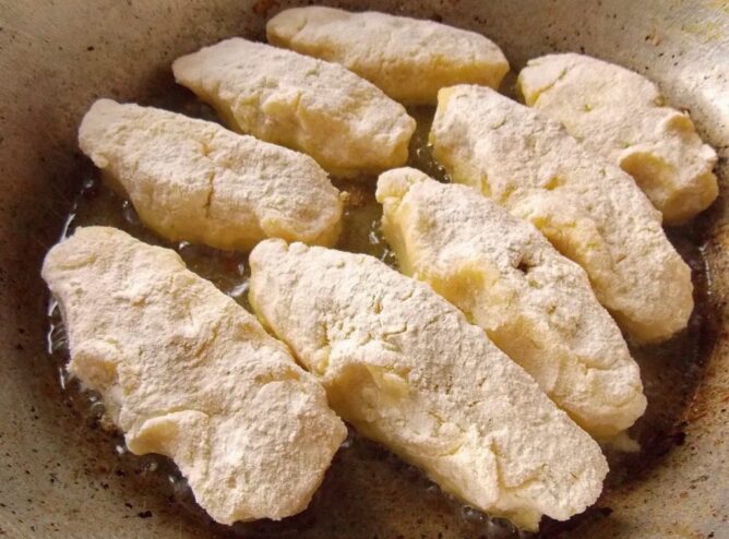 Frying the Potato Zrazy until Golden Raw, formed potato zrazy being placed into a hot frying pan with sizzling oil.