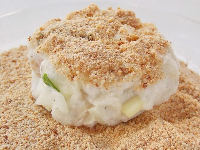 Creating a Crispy Coating with Breadcrumbs A fish cutlet being coated in a dish of breadcrumbs.