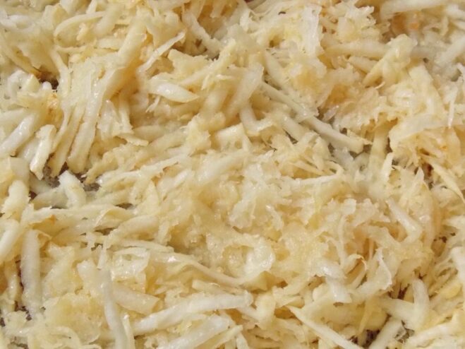 Sautéing grated celery in a pan until soft Grated celery being sautéed in a black frying pan with a wooden spoon.