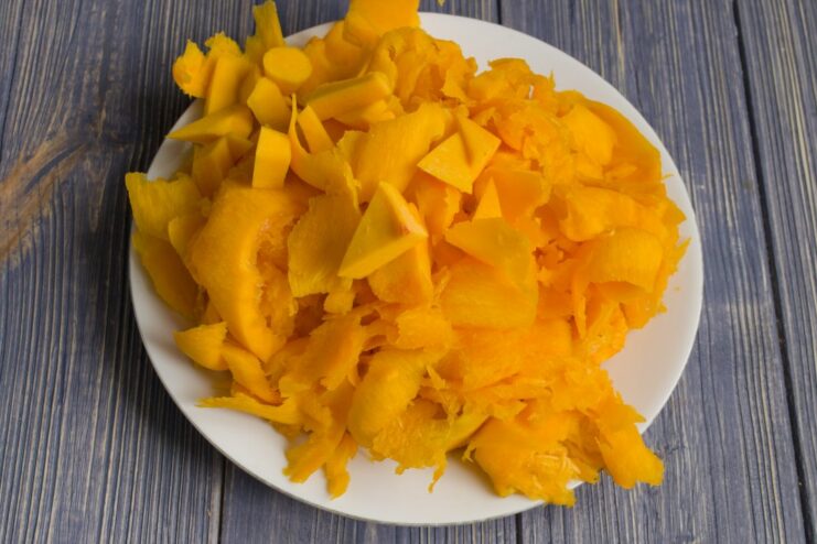 Preparing the Pumpkin for the Stew Hands peeling and chopping a fresh pumpkin on a wooden cutting board.