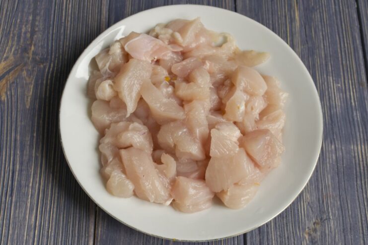 Dicing the Chicken Fillet for the Stew Raw chicken fillet being diced into cubes on a cutting board.