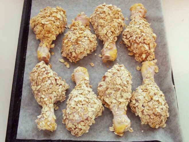 Preparing the cereal-crusted chicken drumsticks for baking on a tray. Raw, cereal-breaded chicken drumsticks arranged on a parchment-lined baking sheet.