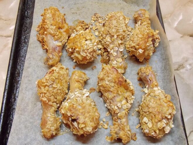 Baking the cereal-crusted chicken drumsticks to a perfect golden brown. Golden-brown baked chicken drumsticks with a crispy cereal crust on a baking sheet.