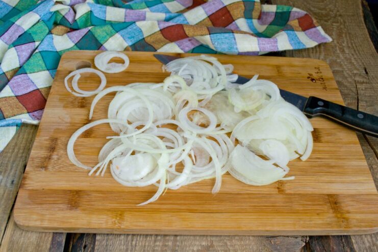 Slicing onions for the Siberian Lecho A white onion being sliced into thin half-rings on a cutting board.