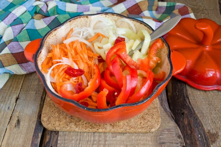 Combining all the vegetables for the Lecho A pot filled with tomato sauce, carrots, onions, and bell peppers, being mixed together.