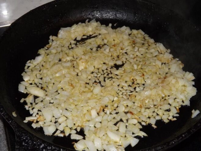Finely chopped onions being sautéed in a frying pan.
