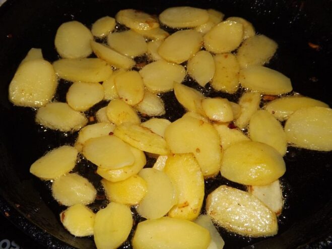 Thin potato slices being fried in a pan.