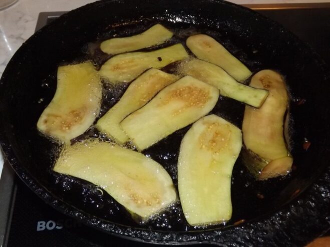 Slices of eggplant being fried in oil in a pan.