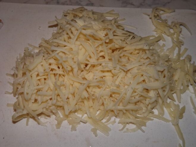 A block of cheese being grated on a coarse grater.