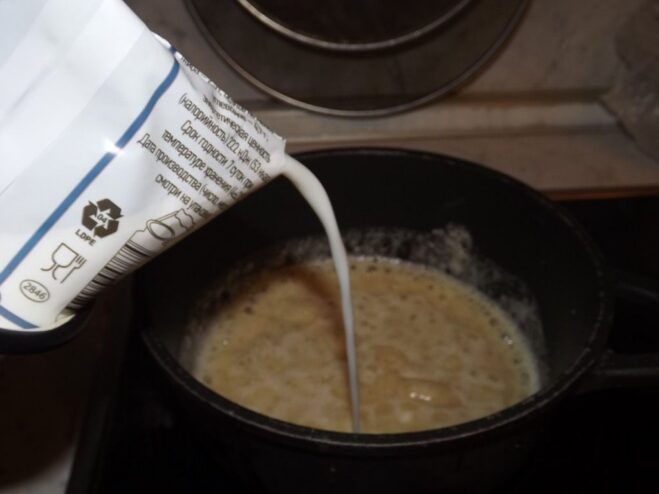 Milk being poured into the flour and butter mixture in a saucepan.