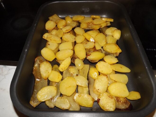 A layer of fried potato slices being arranged in a baking dish.