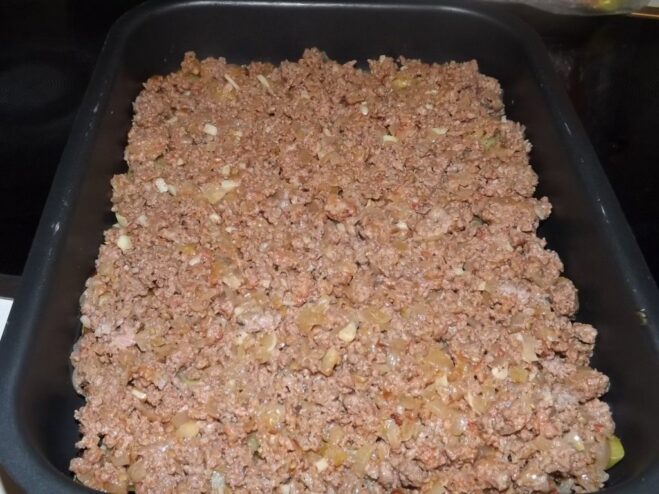 The cooked meat sauce being spread evenly over the potato layer.