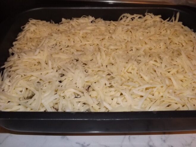 A thick layer of grated cheese covering the meat sauce in the baking dish.