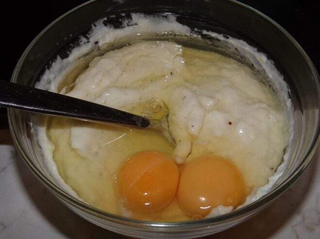 Two eggs being whisked into the creamy béchamel sauce in a bowl.