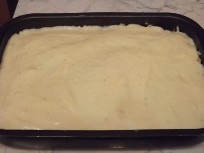 The creamy béchamel sauce being poured and spread over the cheese layer.
