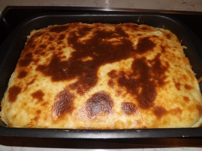 The moussaka in a glass baking dish, baking in the oven.