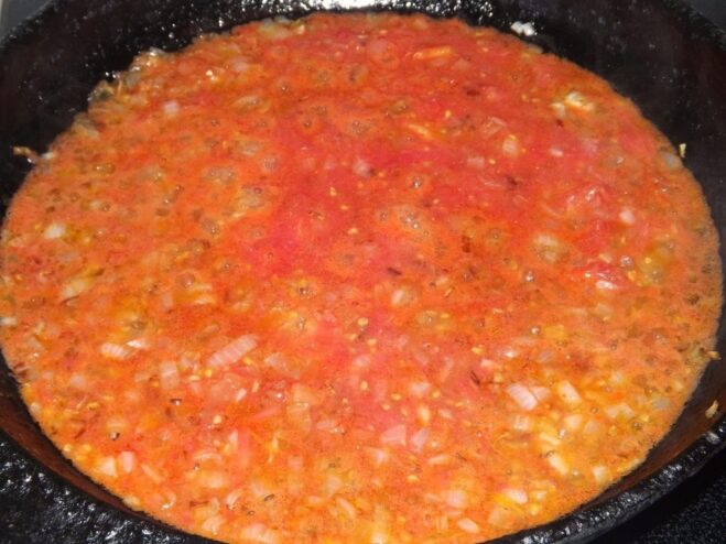 Tomato sauce being added to golden onions in a frying pan.