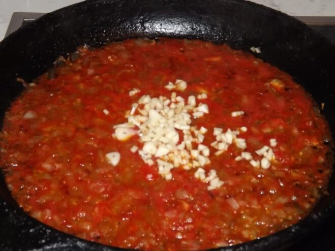 Minced garlic being added to the pan with onions and tomatoes.