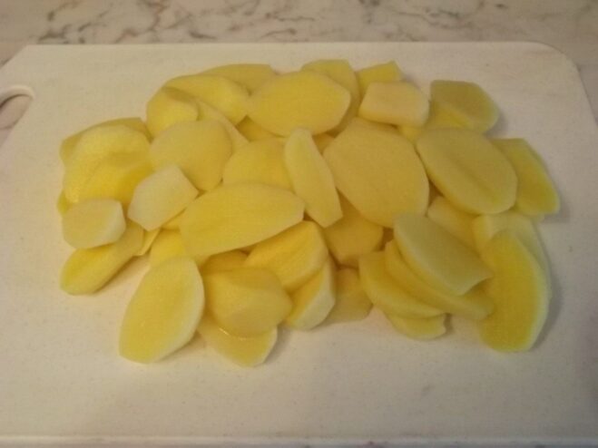 Peeled potatoes being sliced into thin, even rounds.