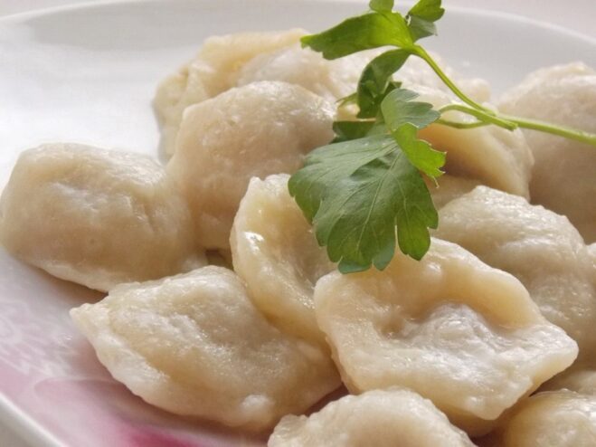 A plate of freshly made, uncooked homemade pelmeni, arranged in neat rows.
