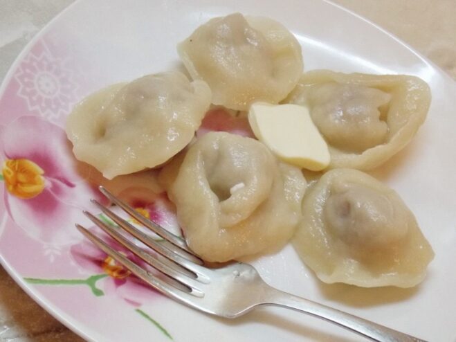 Beautifully Hand-Shaped Homemade Pelmeni A close-up of several beautifully hand-shaped homemade pelmeni on a wooden board.