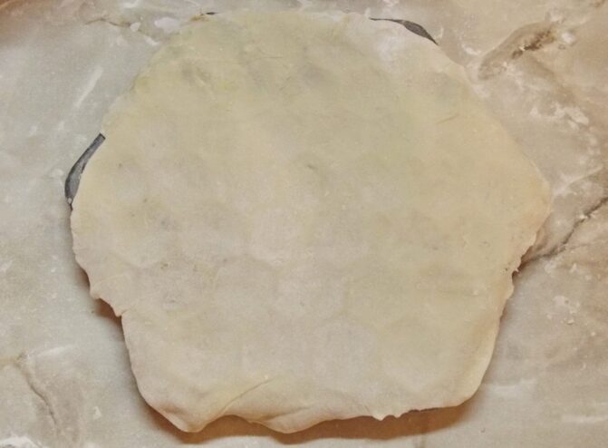 How to Use a Pelmennitsa: Step 1 - Laying the Dough A sheet of thin dough being placed over a metal pelmennitsa (pelmeni mold).