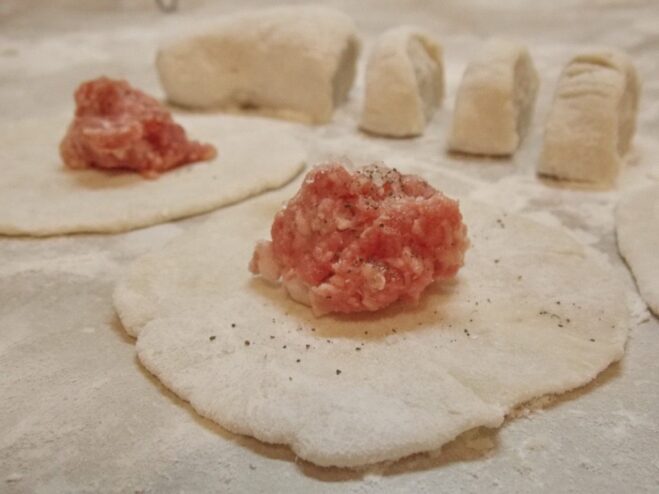 Hand-Shaping Pelmeni: Adding the Filling A small, round piece of dough with a spoonful of meat filling in the center, ready for shaping.