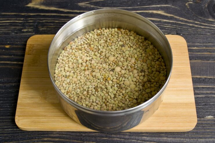 Soaking green lentils in water to soften them before cooking. A bowl of green lentils soaking in clear water.