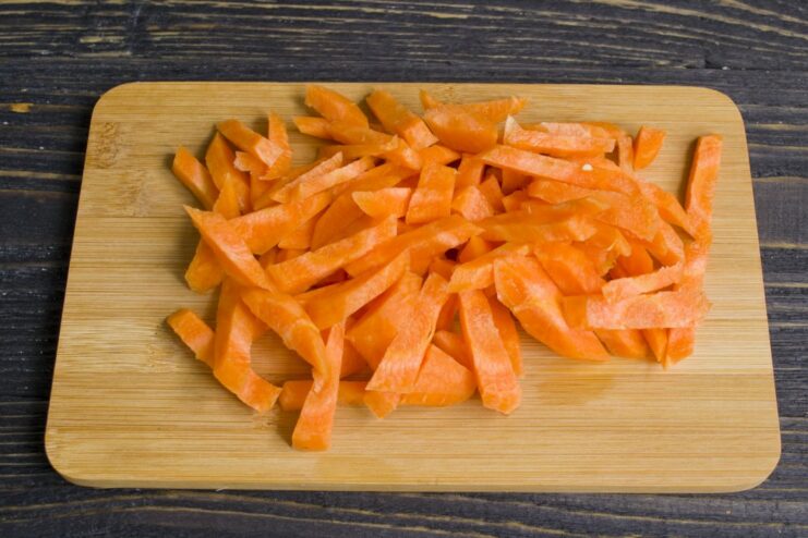 Fresh carrots being chopped into thick batons for the stew. Close-up of carrots being chopped into thick sticks on a cutting board.