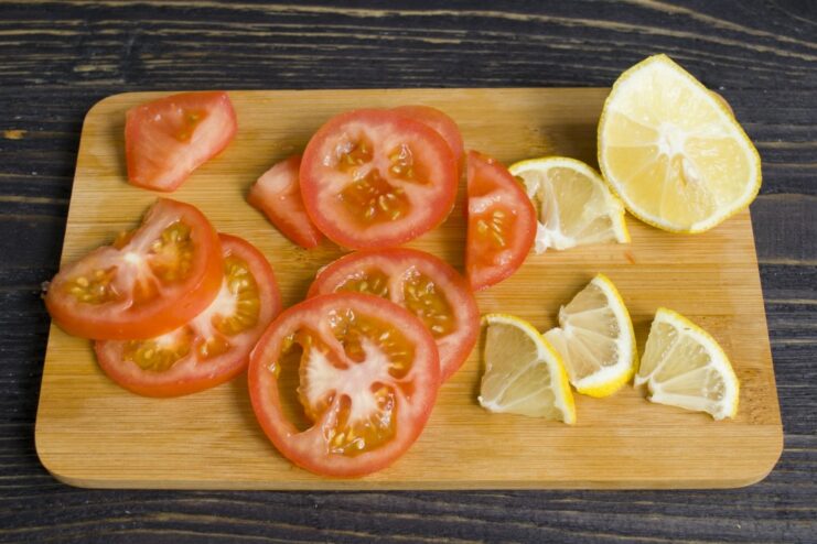 Slicing fresh lemon and tomato to add brightness and acidity to the stew. Thick slices of fresh lemon and red tomato ready to be added to the dish.