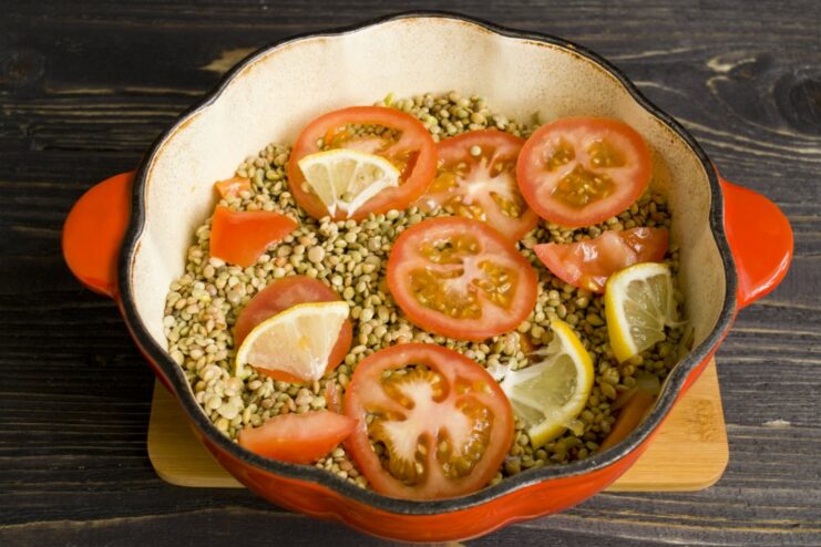 Final layers before simmering: lentils, tomato, and lemon slices arranged over the chicken. Lentils, tomato slices, and lemon slices layered over chicken and vegetables in a pot.
