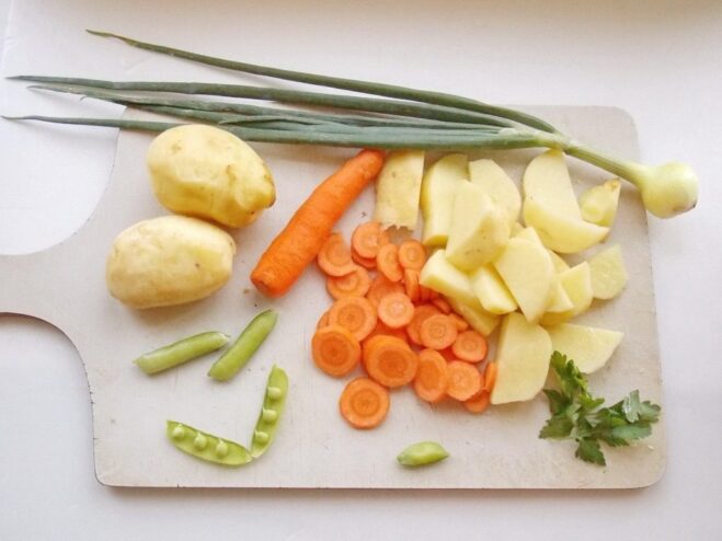 Preparing fresh young vegetables for the summer stew. A collection of freshly chopped vegetables like potatoes, carrots, and zucchini on a cutting board.