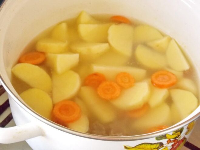 Starting the stew by cooking potatoes and carrots in a pot. Chopped potatoes and carrots simmering in a pot of water, the first step of making the stew.