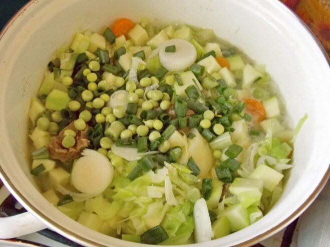 Adding fresh green peas and chopped onion to the stew for more flavor. Fresh green peas and chopped onions being added to the simmering vegetable stew in a pot.