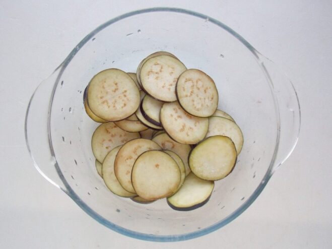 How to Prepare Eggplant to Remove Bitterness Sliced eggplant in a bowl, sprinkled with coarse salt to draw out moisture and bitterness.